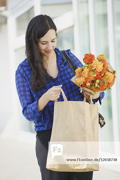 Lächelnde Frau hält Blumenstrauß  während sie in Papiertüte schaut.