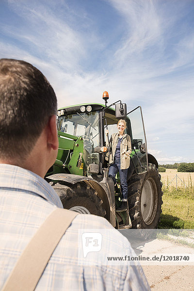 Smiling woman standing on tractor while looking at man against sky