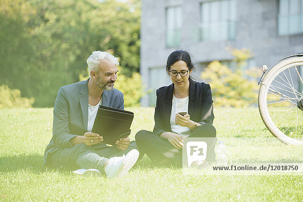 Business colleagues discussing while sitting on grass field