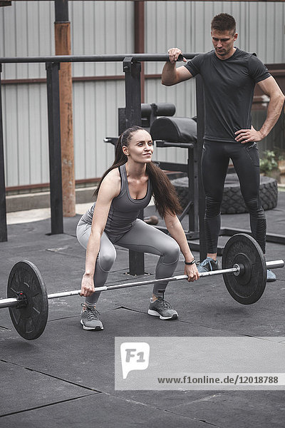 Male instructor looking at female athlete lifting barbell during cross training