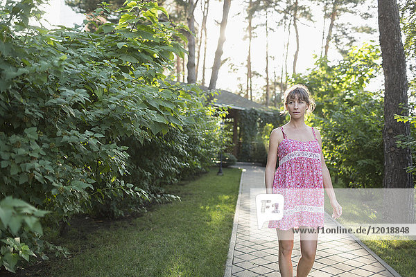 Frau in rosa Kleid auf dem Weg inmitten von Pflanzen im Hof