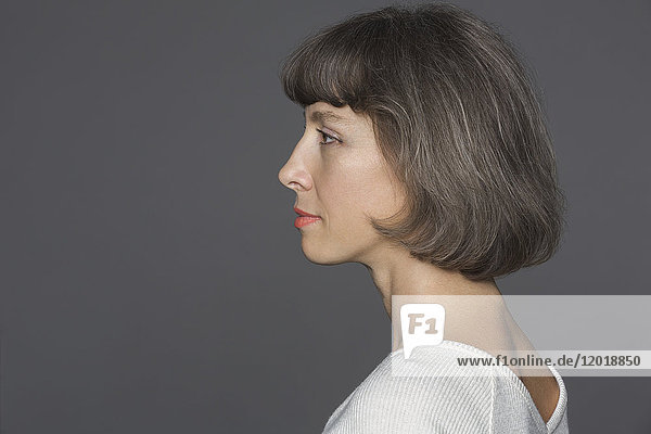 Seitenansicht der reifen Frau mit braunen Haaren vor grauem Hintergrund