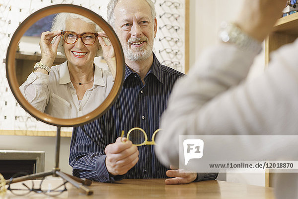 Optikerin unterstützt lächelnde Frau bei der Brillenauswahl im Geschäft