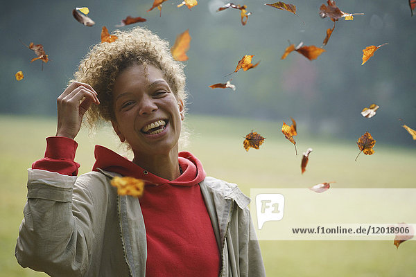Porträt einer fröhlichen Frau mit Hand im Haar inmitten von Herbstblättern