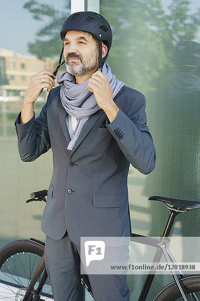 Mature businessman wearing cycle helmet while standing against glass window