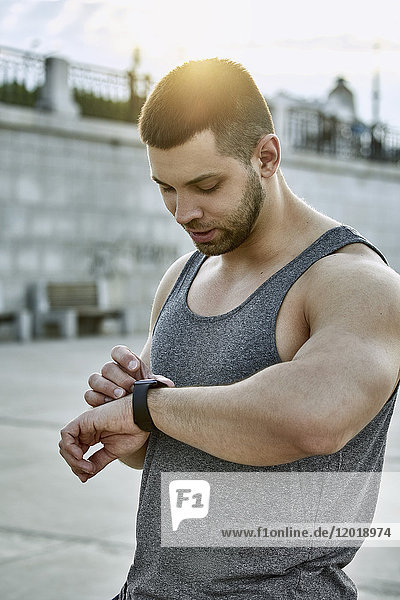 Männlicher Sportler mit intelligenter Uhr im Stehen am Fußweg