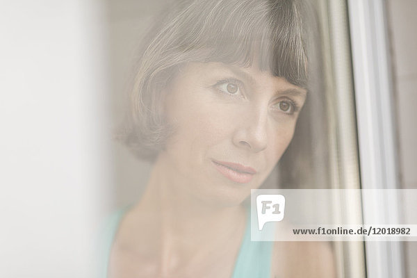 Close-up of thoughtful mature woman seen from window glass