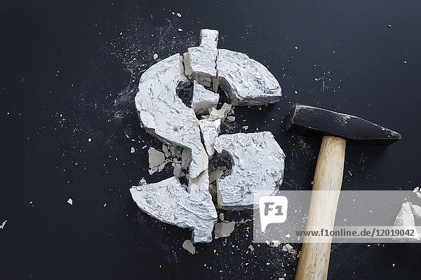 Hochwinkelansicht des gebrochenen Betons Dollarzeichen mit Hammer auf dem Tisch