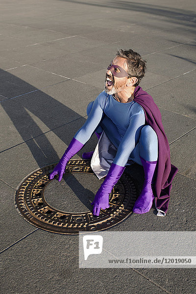 Großer Blickwinkel auf das Schreien des Superhelden beim Öffnen des Mannlochdeckels auf dem Fußweg in der Stadt