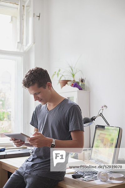 Young male university student using digital tablet at home