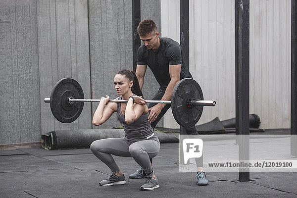Male instructor assisting young woman crossfit training at gym