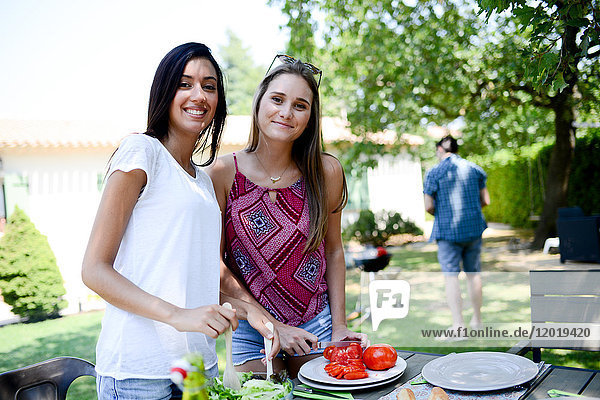 Zwei schöne junge Frauen im Garten bereiten Tomatensalat für eine Grillparty im Sommerurlaub vor.