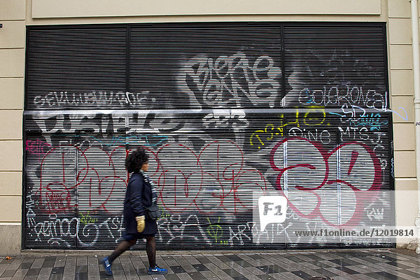 Frankreich  Paris  Frau geht vor einem mit Graffiti bedeckten eisernen Vorhang.