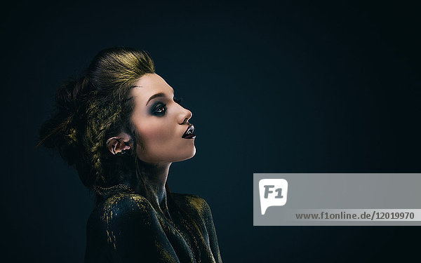 Portrait of a young woman in profile  the body painted black and gold  the look on the side