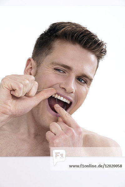 Oben-ohne-Mann  der in den Spiegel schaut und seine Zähne mit Zahnseide putzt.