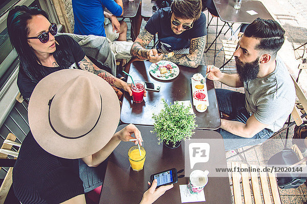 Gruppe junger Hipster  die auf einer Restaurantterrasse sitzen  essen und trinken