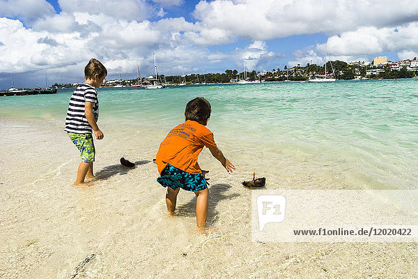 Two young boys  5 and 7 years old  playing with small boat in coco ont he beach  Gosier island  Guadeloupe  France