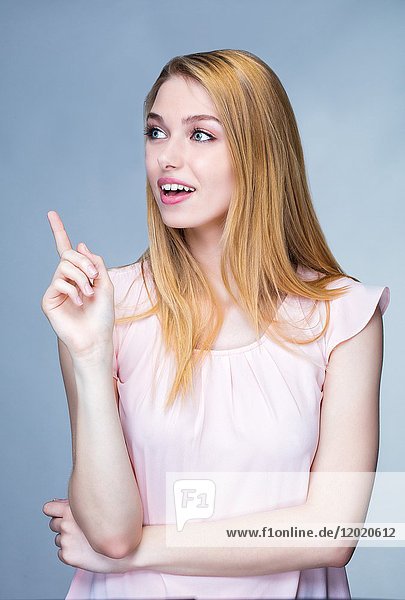 Porträt einer lächelnden jungen Frau mit erhobenem Finger an der Seite