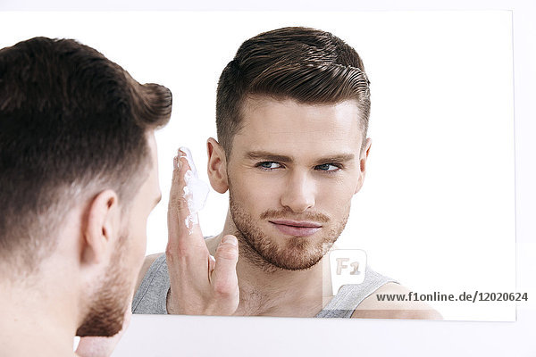Mann im Unterhemd  der lächelnd in den Spiegel schaut  mit Rasiergel auf der Hand