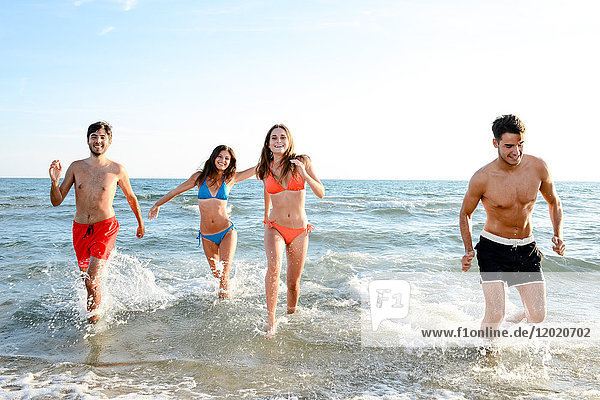 Frankreich  vier junge Erwachsene  die im Badeanzug im Meer laufen.