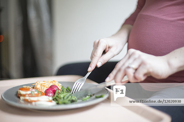 Nahaufnahme einer schwangeren Frau  die einen Teller mit Salat und Gemüse isst.