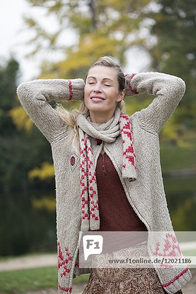 Porträt einer jungen blonden Frau  die mit den Armen über dem Kopf in einem Wald im Herbst frische Luft atmet.