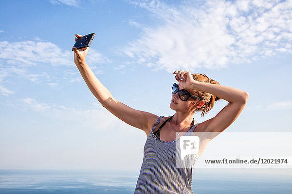 Porträt einer jungen Frau im Profil  die ein Selfie mit ihrem Smartphone auf den Höhen von Setubal  Lissabon und Umgebung  Portugal  macht