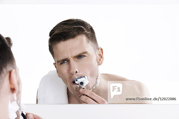 Oben-ohne-Mann  der in den Spiegel schaut  seinen Schnurrbart rasiert  seinen Bart rasiert  mit Rasiermesser in den Händen  rasiert