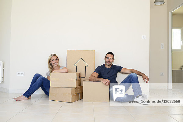 Ein glückliches junges Paar trägt Kartons und zieht in sein neues Haus ein.