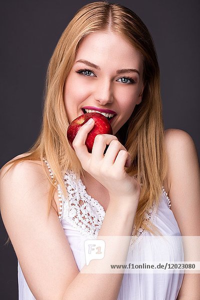 Porträt einer lächelnden jungen Frau  die in einen Apfel beißt