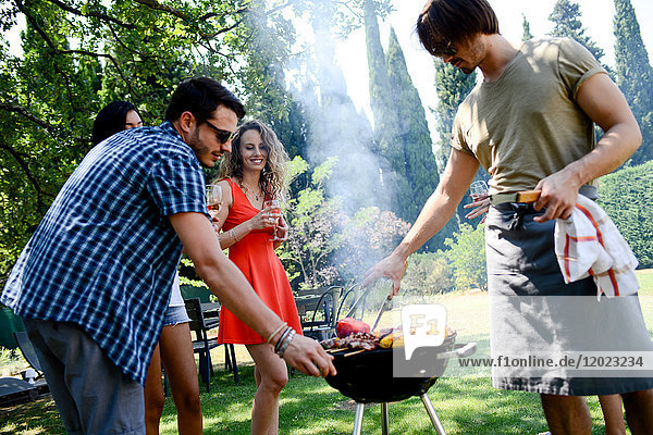 Groupe of happy and cheerful young people having fun around barbecue grill during summer holiday party outdoor in the garden.