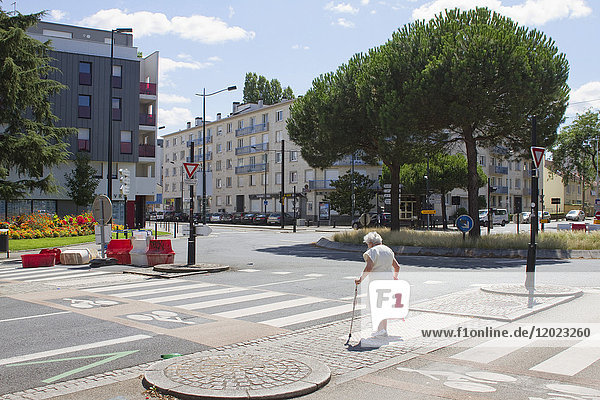 Frankreich  Nantes  alte Frau  die im Sommer eine einsame Straße überquert.