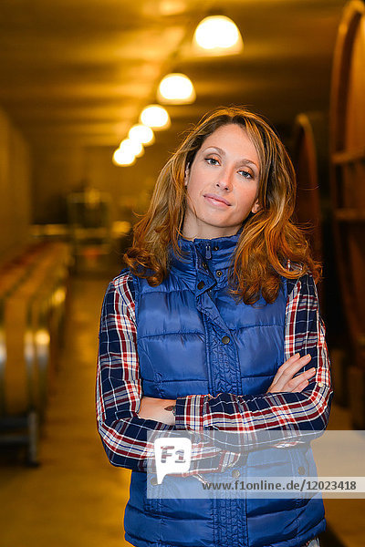 Fröhliche junge Winzerin posiert in ihrem Keller mit einem Weinfass im Hintergrund - Cepage Grenache  Chateauneuf du Pape  cotes du Rhone  Frankreich