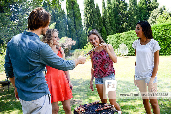 Eine Gruppe glücklicher und fröhlicher junger Leute,  die sich während einer Sommerferienparty im Garten am Grill vergnügen.