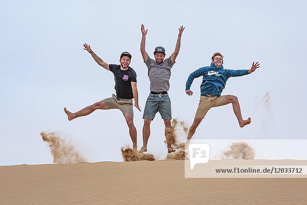 Three young men jumping in the sand  Namib Desert  Namibia  Africa