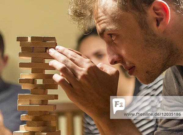 Junger Mann spielt Jenga  stapelt einen Turm mit Holzklötzen  konzentriert