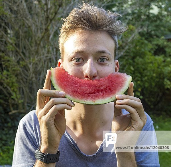 Young man holding a melon as mouth in front of his face  Bavaria  Germany  Europe