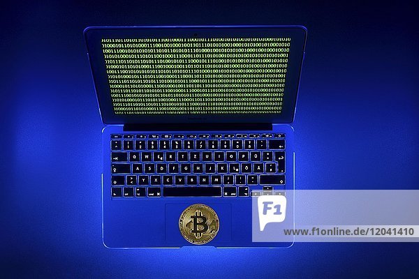 Symbolbild digitale Währung  goldene physische Münze Bitcoin Laptop mit digitalem Binärcode