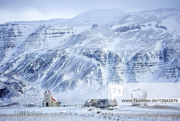 Kirche und abgelegener Bauernhof vor schneebedeckten Bergen  Winternachmittag auf der Straße zur Snaefellsnes-Halbinsel  Island  Polarregionen