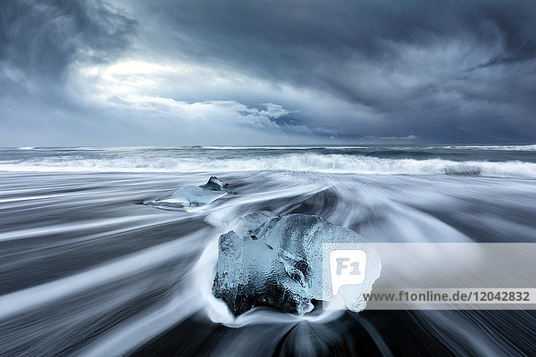 Gletschereis auf schwarzem Sandstrand mit Wellen  die an einem stürmischen Wintertag an den Strand gespült werden  nahe Jokulsarlon  Südisland  Polarregionen