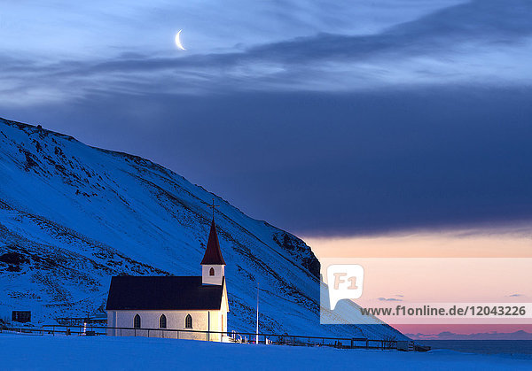 Beleuchtete Kirche in der Morgendämmerung vor schneebedeckten Bergen  Winter  bei Vik  Südisland  Polarregionen