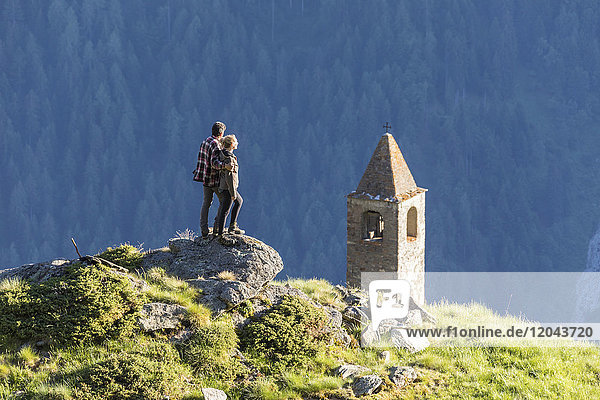 Mann und Frau umarmt Blick auf den Glockenturm  San Romerio Alp  Brusio  Poschiavo Tal  Kanton Graubünden  Schweiz  Europa