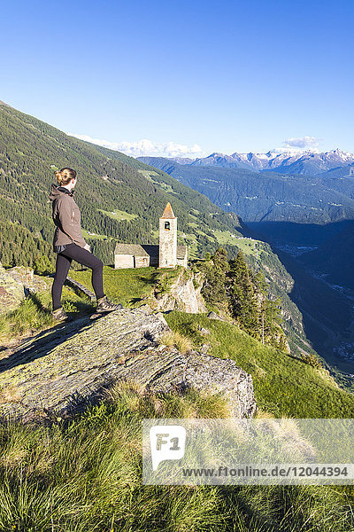 Frau blickt auf alte Kirche in den Bergen  Alp San Romerio  Brusio  Kanton Graubünden  Poschiavo-Tal  Schweiz  Europa