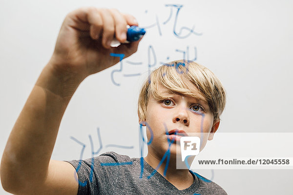 Close up of boy's hand writing equation onto glass wall