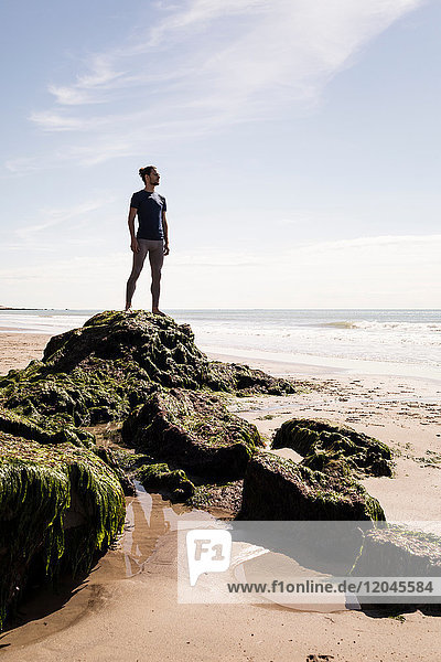 Junger männlicher Läufer schaut vom Strandfelsen aufs Meer hinaus