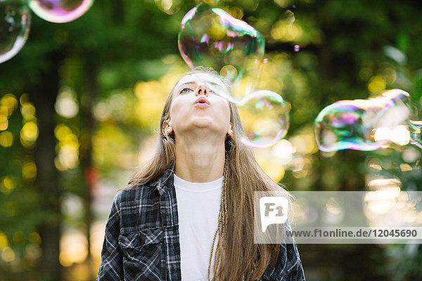Junge Frau bläst im Park schwebende Blase nach oben