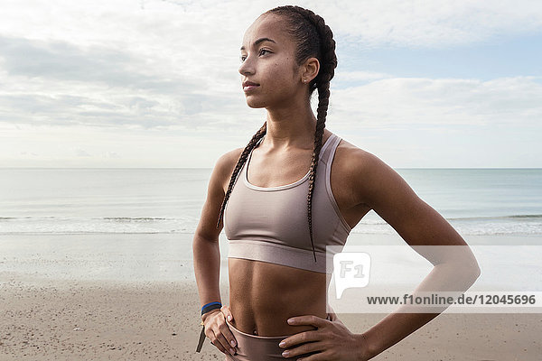 Young female runner with hands on her hips at beach