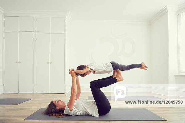 Mother and daughter in yoga studio  daughter balancing on mothers legs