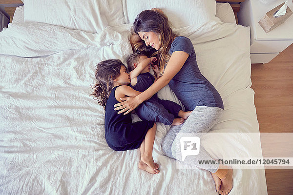 Mutter und zwei kleine Kinder  auf dem Bett liegend