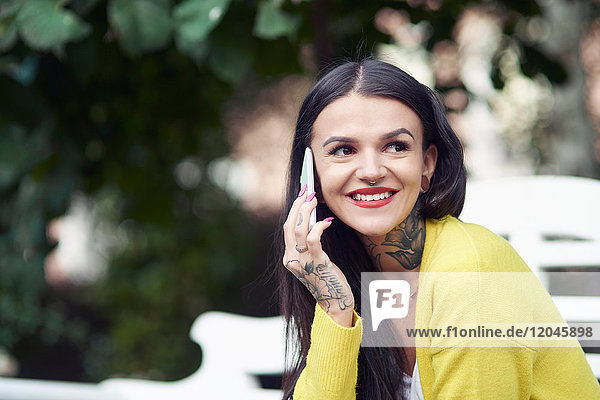 Young woman sitting outdoors  using smartphone  smiling  tattoos on hand and neck
